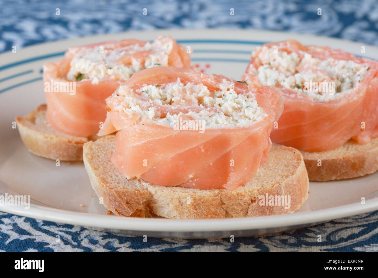 smoked salmon rolled around cheese and herb filling on toasted french bread appetizers on a plate viewed from the front Stock Photo