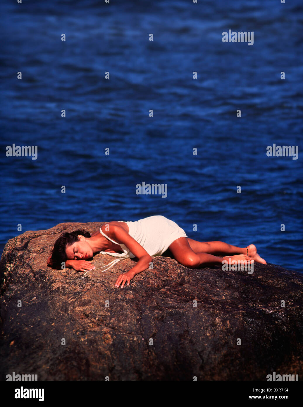 Young woman lying on stone. Ocean in background.20s, 30s, 25-29, 30-34, years old Stock Photo