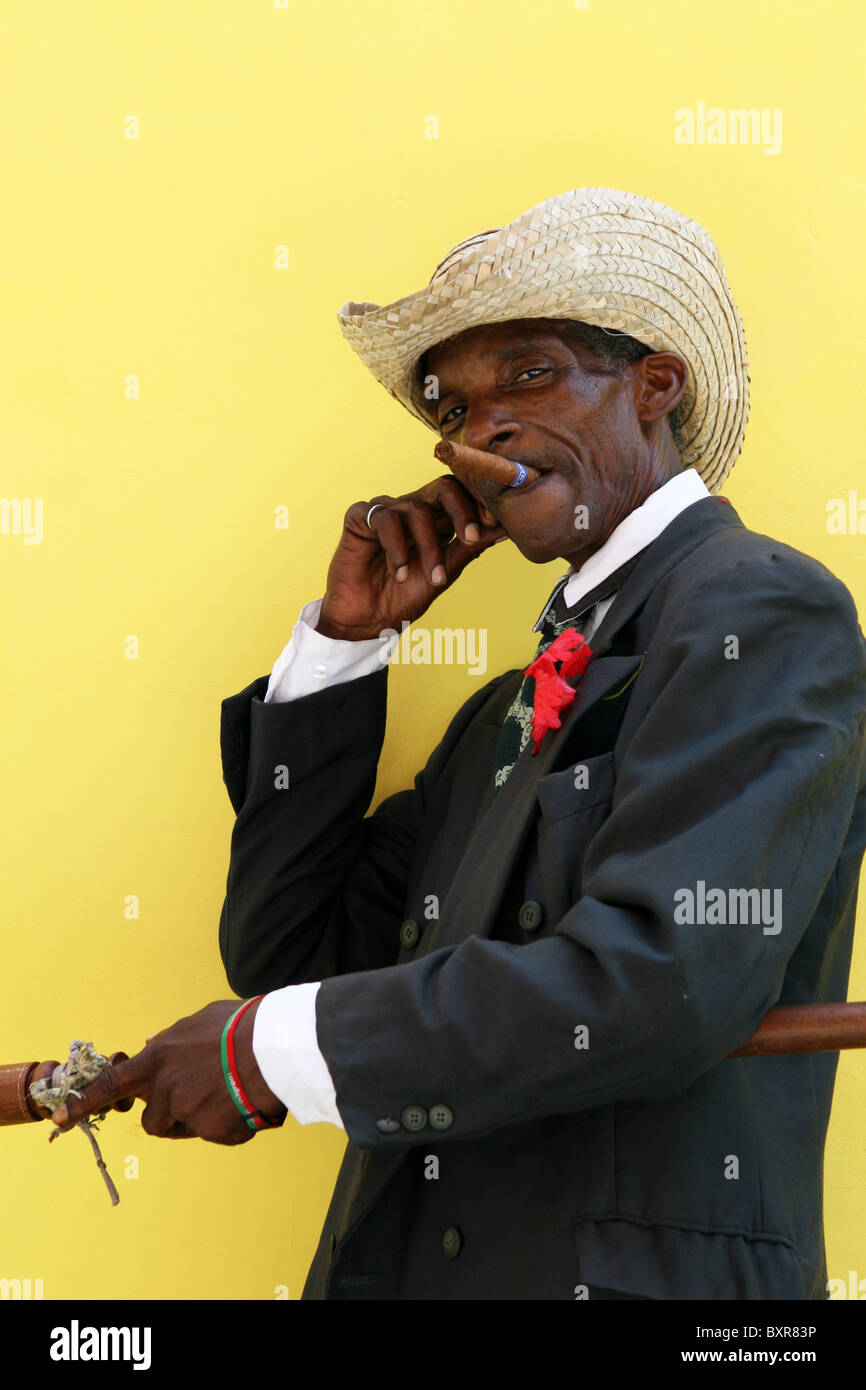 Old man posing with straw hat, walking stick and cigar, against a