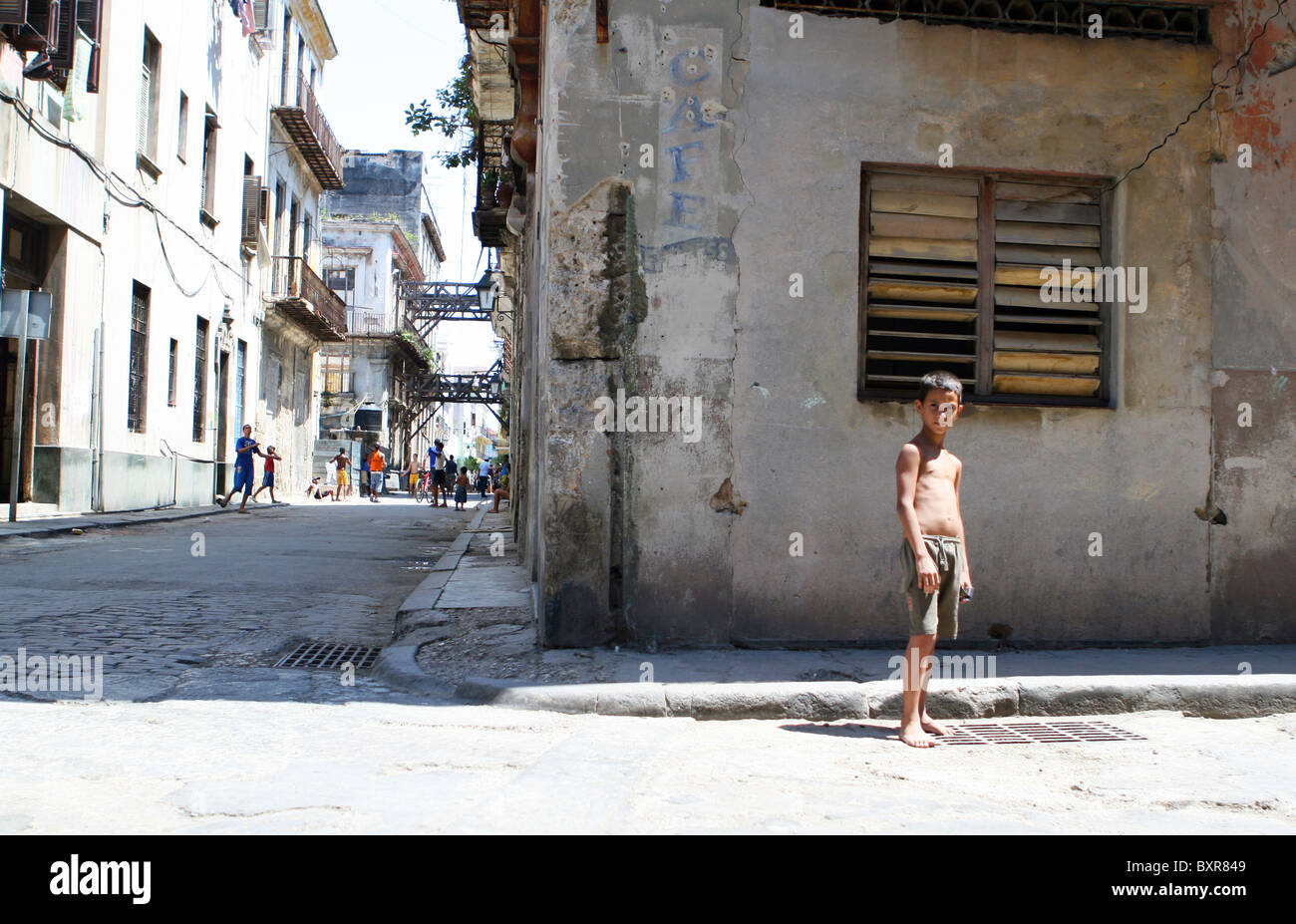 Cuban boy standing in a back street with other kids playing football in the old town, Havana, Cuba. Stock Photo