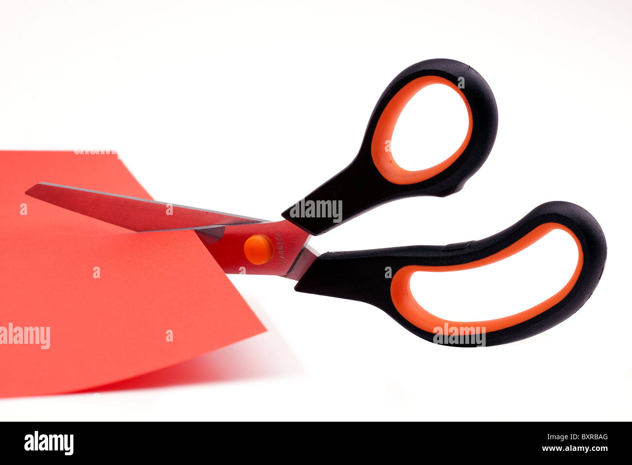 Scissors cutting through a sheet of red paper Stock Photo