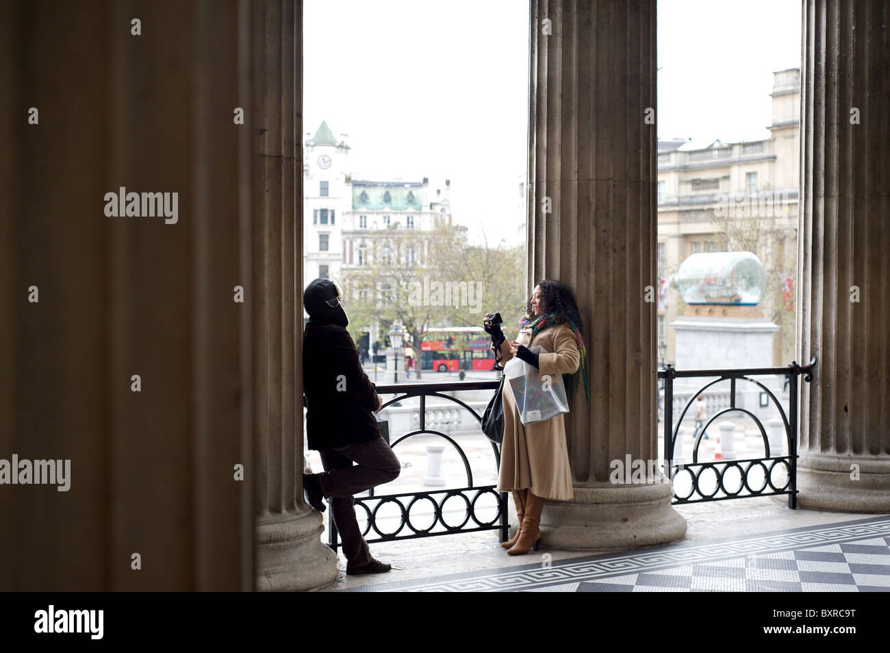 A lady photographing her boyfriend in the entranceway to the National Gallery, Trafalgar Square, London, England, UK Stock Photo
