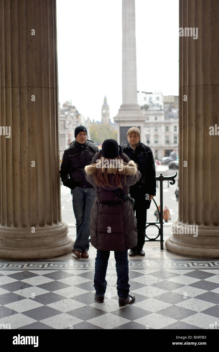 A lady photographing her two friends in the entranceway to the National Gallery with Big Ben in the distance, London, England Stock Photo
