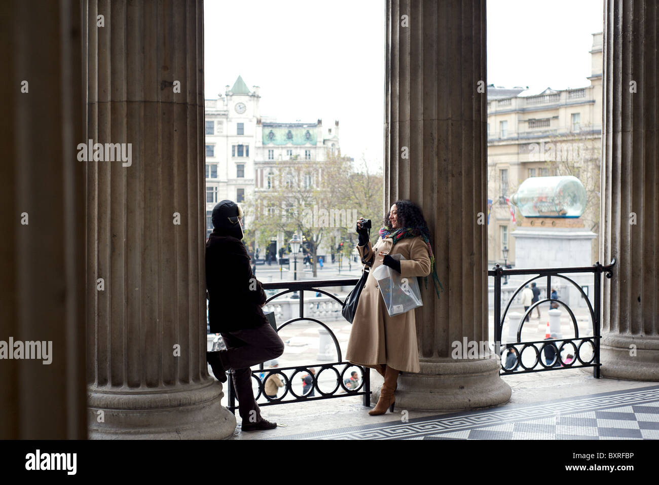 A lady photographing her boyfriend in the entranceway to the National Gallery, Trafalgar Square, London, England, UK Stock Photo
