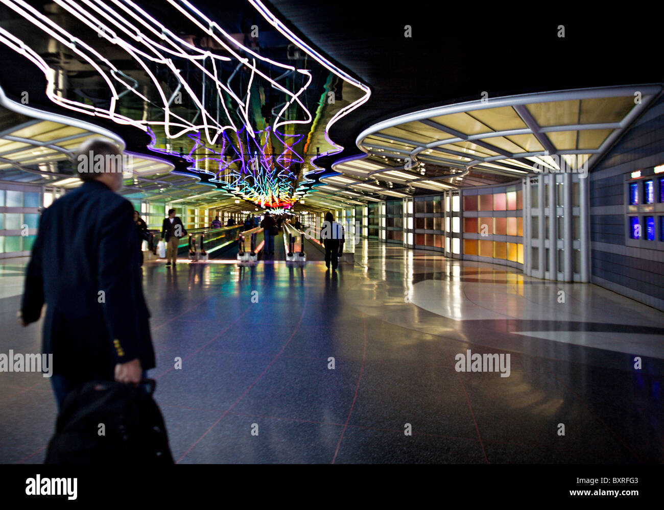 CHICAGO, ILLINOIS: Busy travelers on a moving sidewalk illuminated by colored neon lights in the underground tunnel Stock Photo