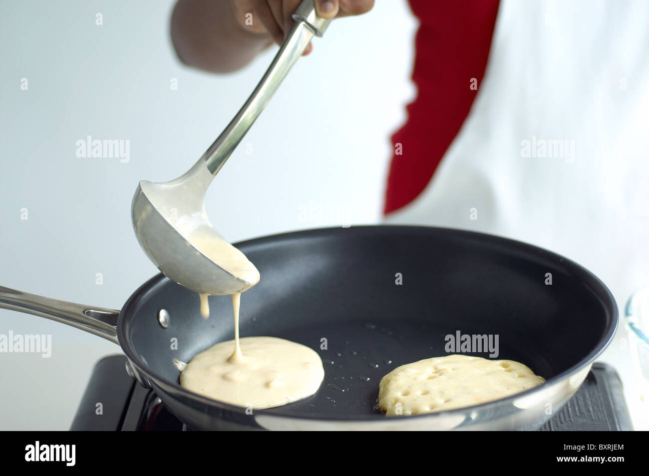 Hand holding ladle, pouring batter into frying pan, closeup Stock