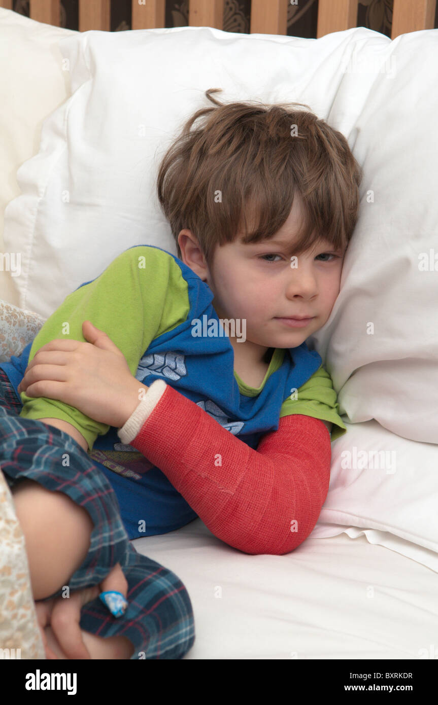 Fouryearold boy with broken arm laying in bed. Red plaster cast Stock