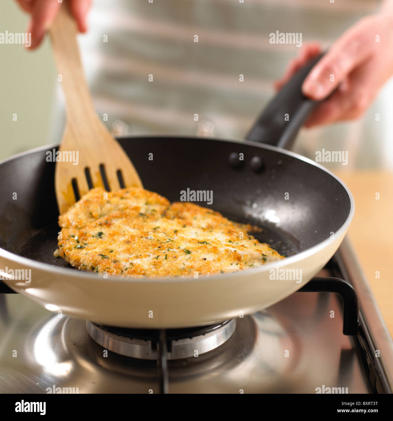 Wooden spatula flipping chicken escalope in frying pan Stock Photo