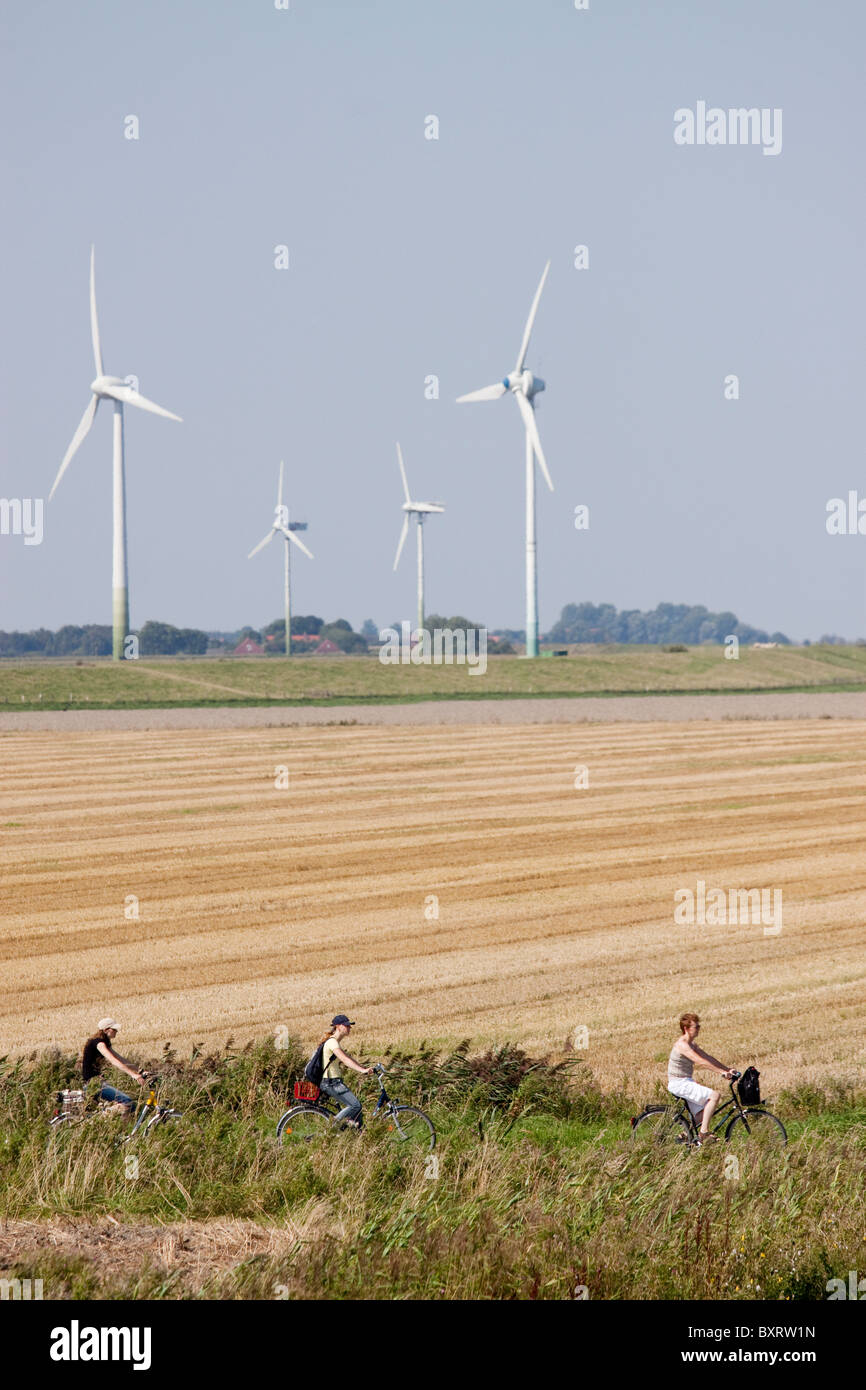 Germany, Ostfriesland (East Frisia), People cycling through field with wind turbines in background Stock Photo