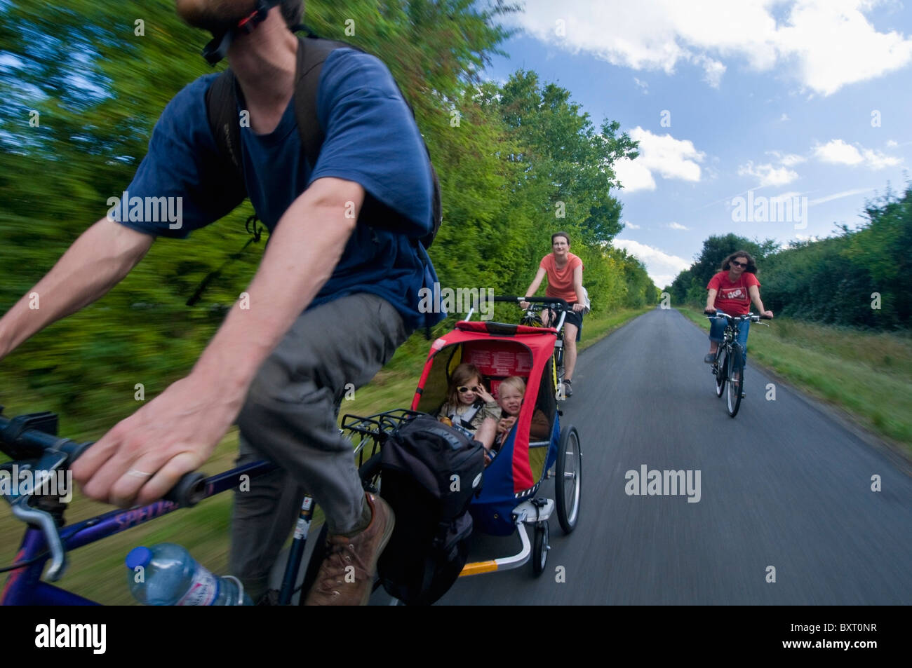 Two Women And Man Cycling With Chariot With Two Young Children (8-9) Stock Photo
