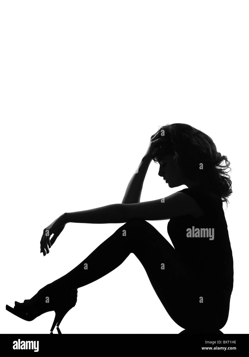 full length silhouette in shadow of a young woman sitting sad pensive in studio on white background isolated Stock Photo