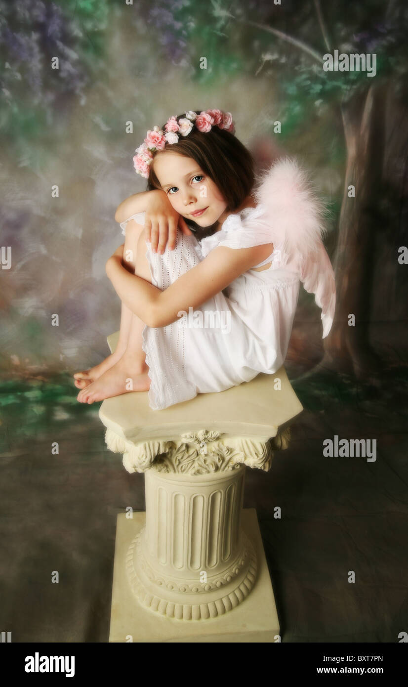 Beautiful young girl wearing pink angel wings and flower halo sitting on a pedestal Stock Photo