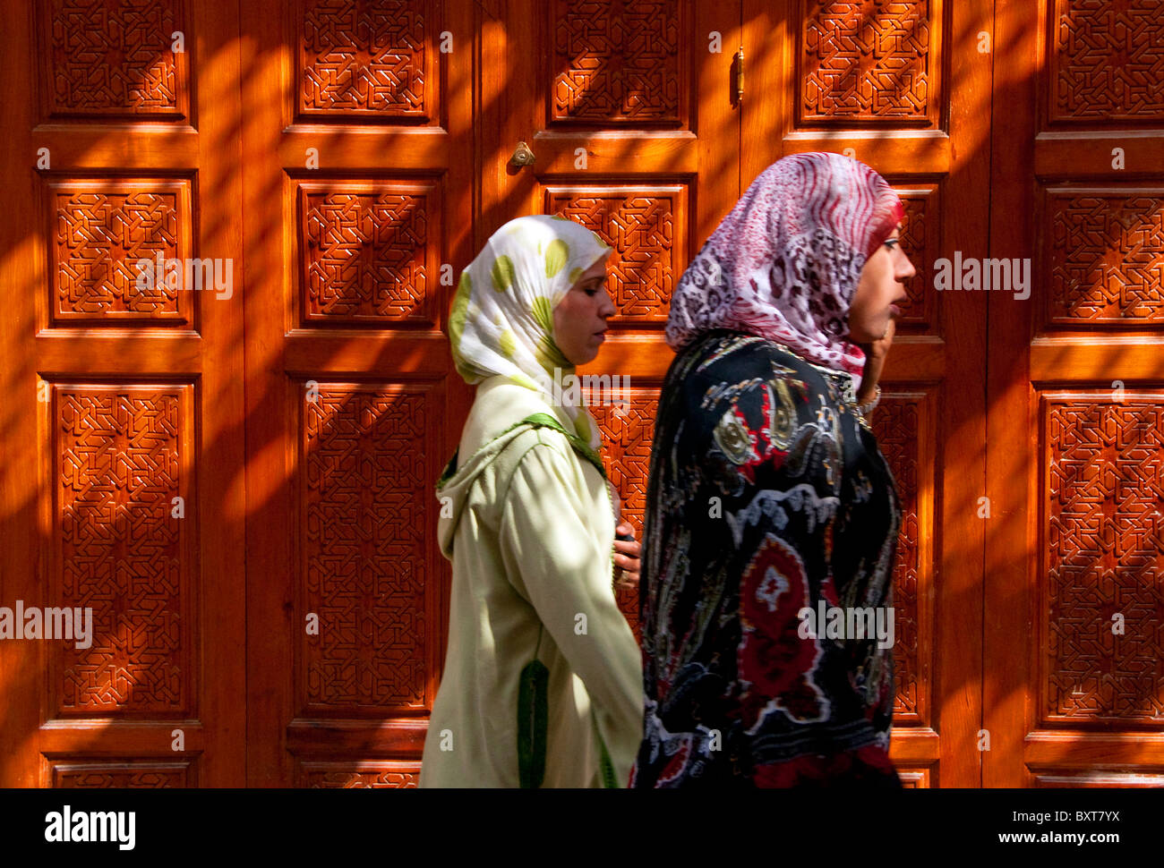 Muslim women passing carved door in old medina of Fes, Morocco Stock Photo