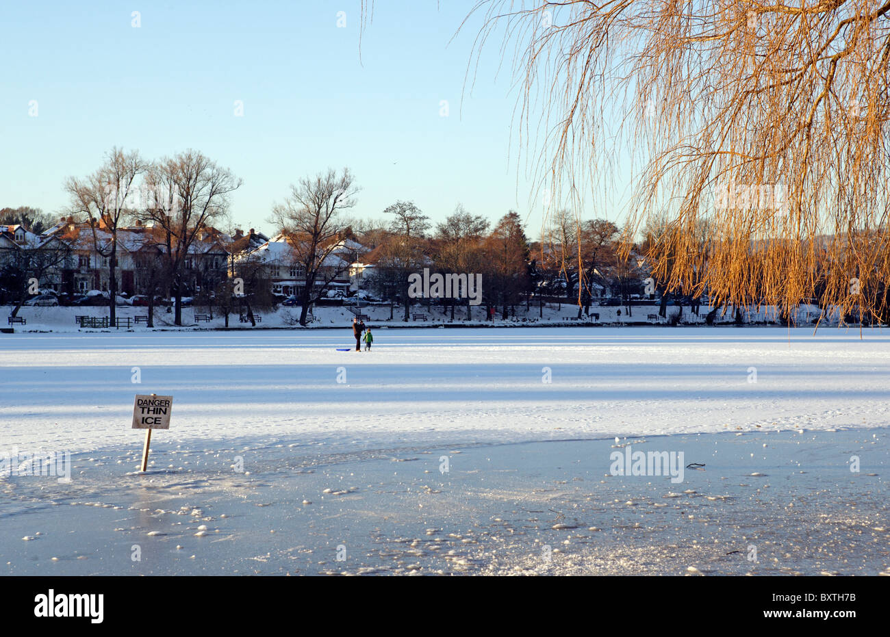 mother and children walking across a frozen lake despite the signs warning of thin ice Stock Photo