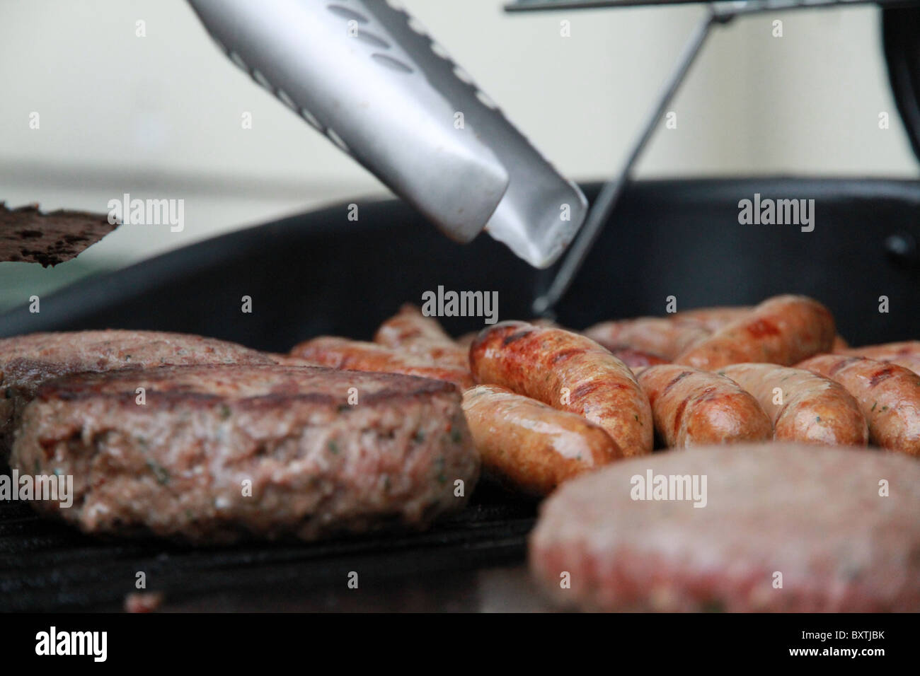 Closeup of sausages and burgers being cooked on a bbq hotplate Stock Photo