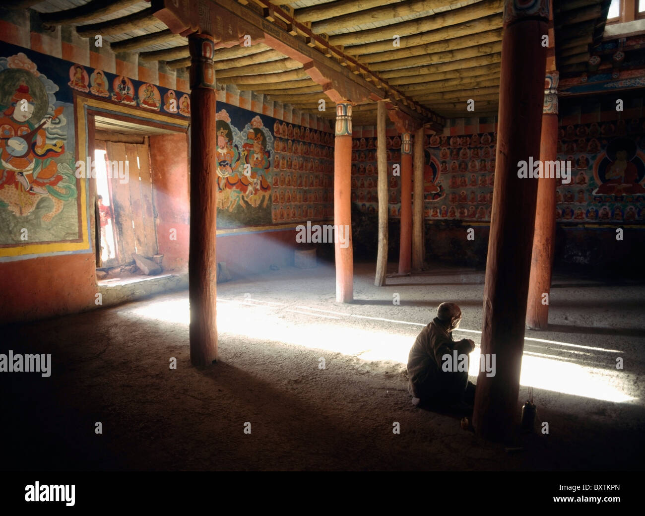 Old Man Praying In Tsemo Monastery With Ray Of Light Coming Through Doorway Stock Photo