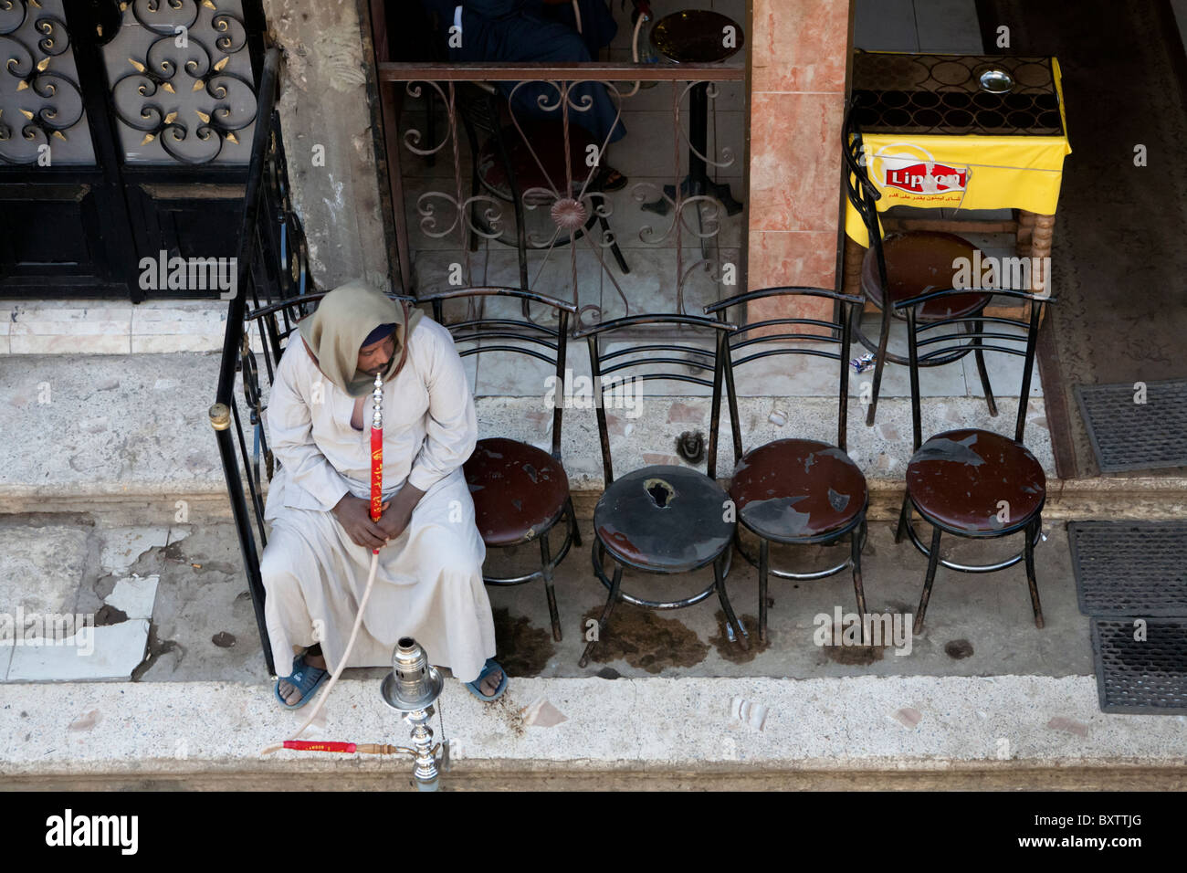 Lone man sitting on the end of a row of five chairs smoking a shisha at a local street market, Luxor, Egypt, Africa Stock Photo
