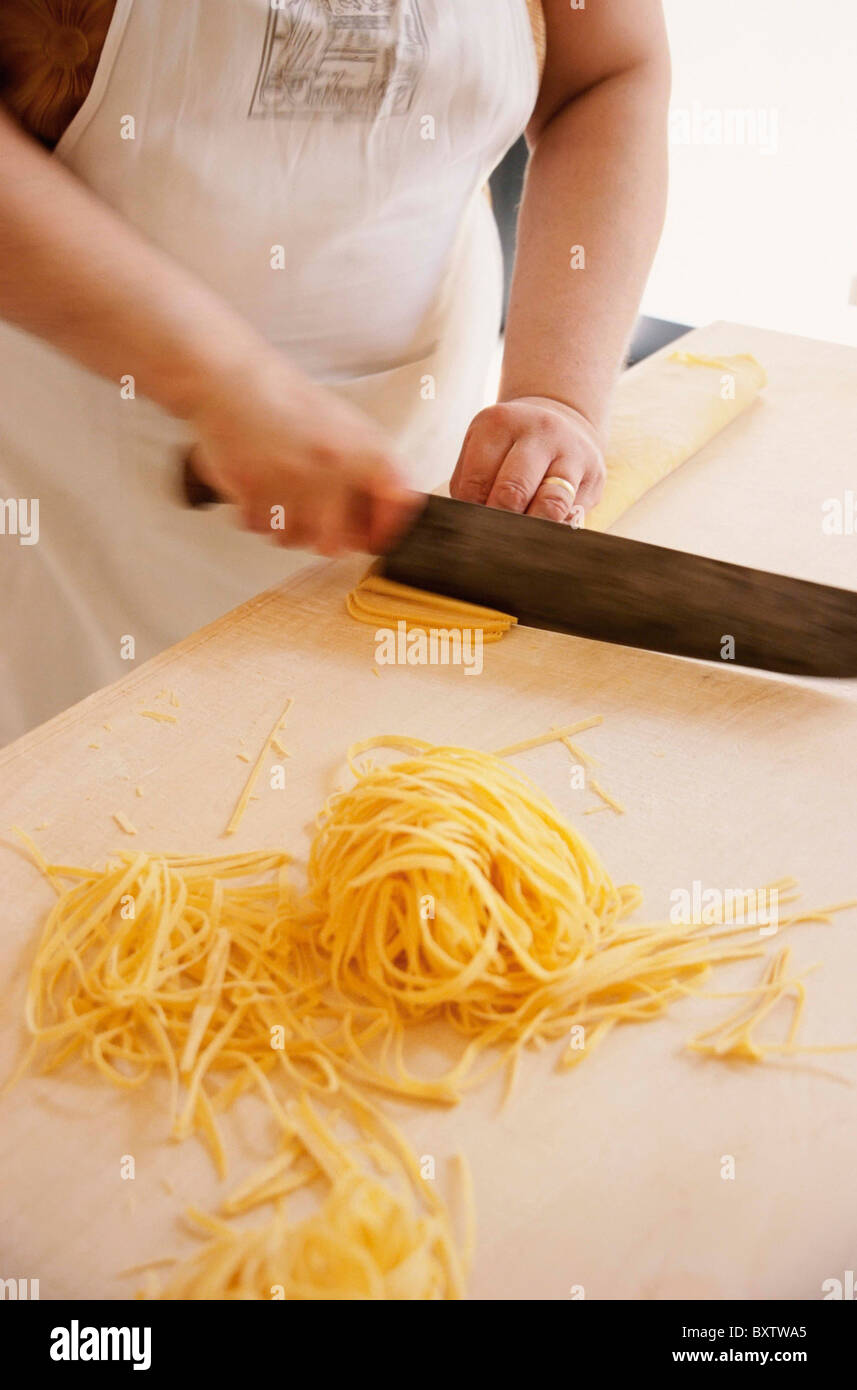 Cook Making Tagliatelli Pasta By Cutting Rolled-Up Sheet Of Pasta , La Vecchia Scuola Stock Photo