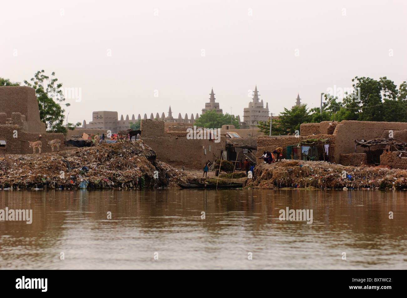 Mounds of household refuse on the banks of the Bani river in Djenné. The Great Mosque on the background. Djenné, Mali. Stock Photo