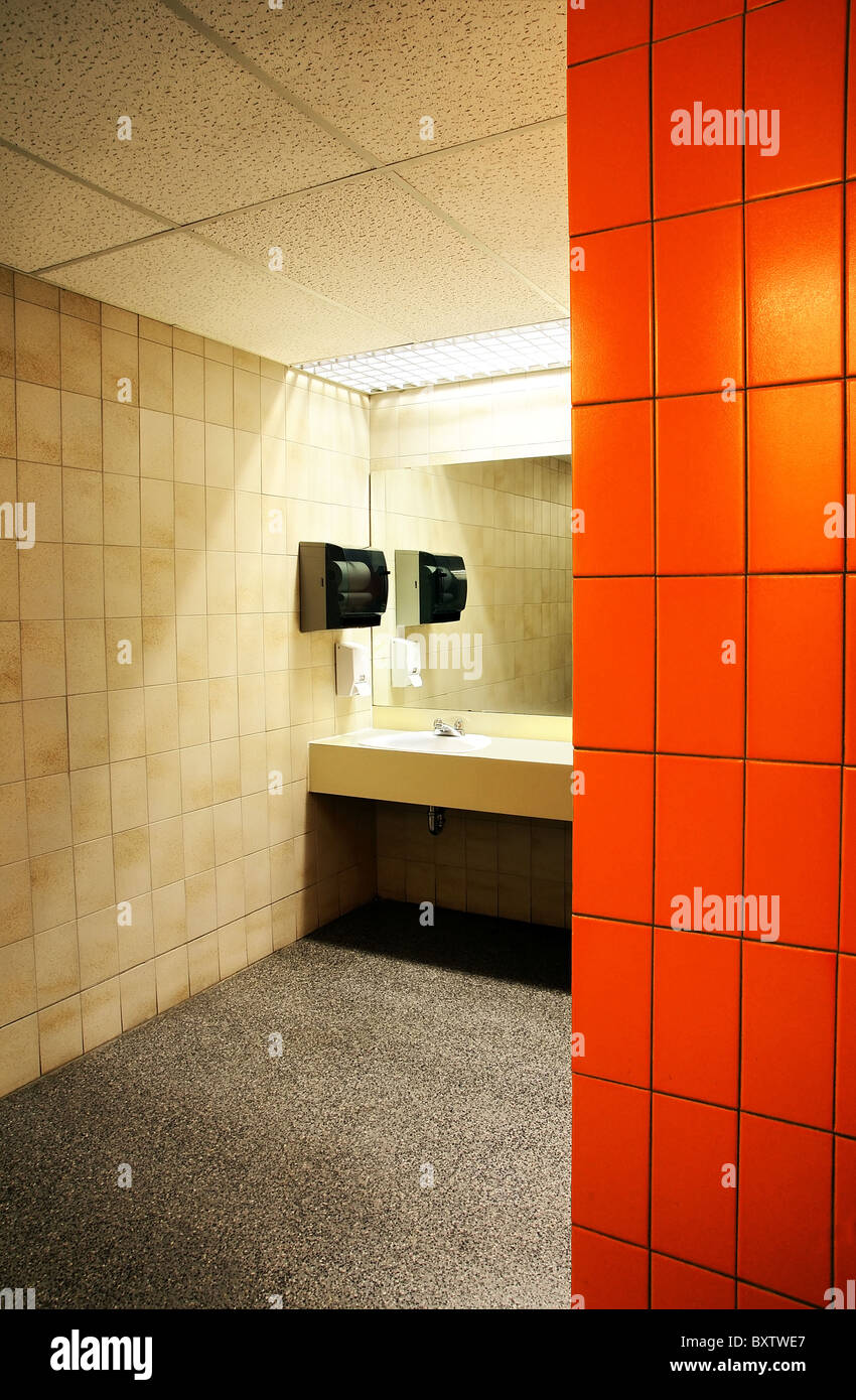 sink behind the orange tile wall of a public bathroom Stock Photo