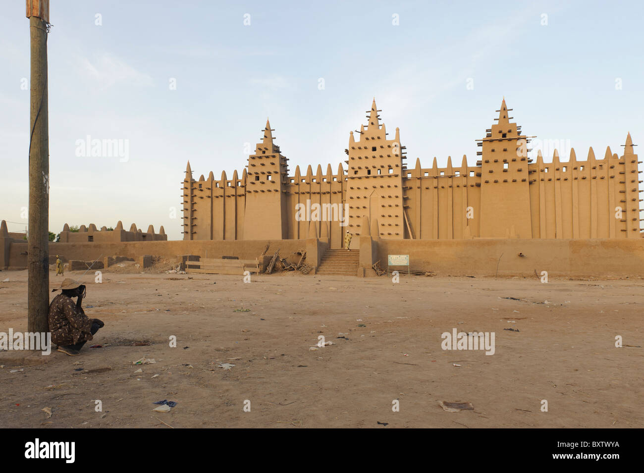 Man leaning against a lamppost and listening at a transistor radio beforeThe Great  Mosque of Djenné, Mali, early in the morning Stock Photo