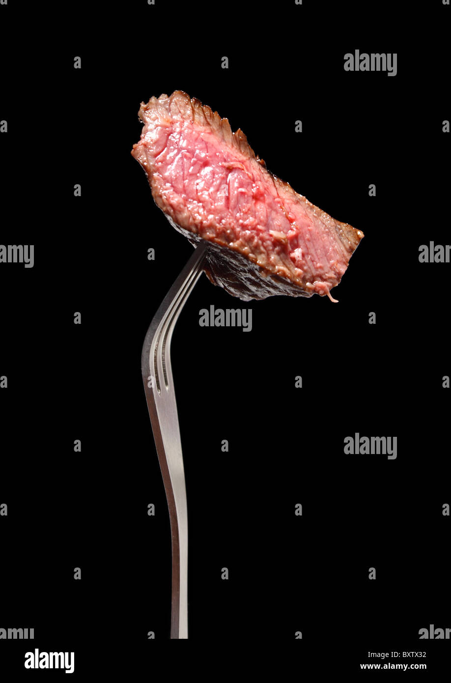 A piece of grilled steak on a fork, isolated on black. Stock Photo