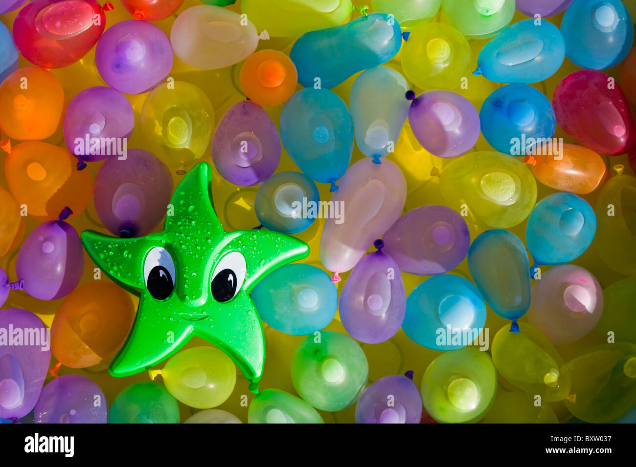 Green toy star with eyes floating between colored water filled ballons Stock Photo