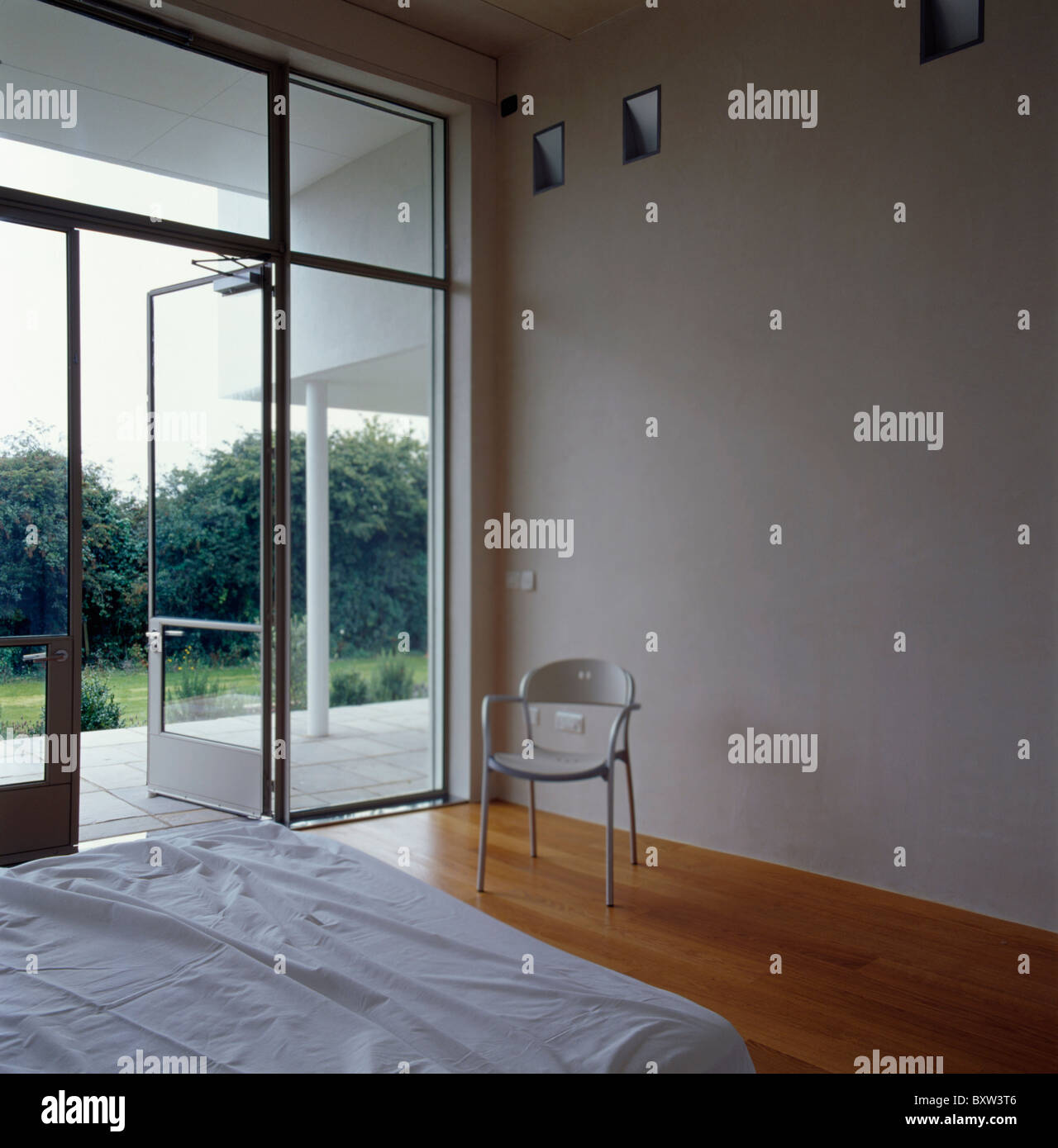 Small White Chair Beside Floor To Ceiling Window And Glass Door In