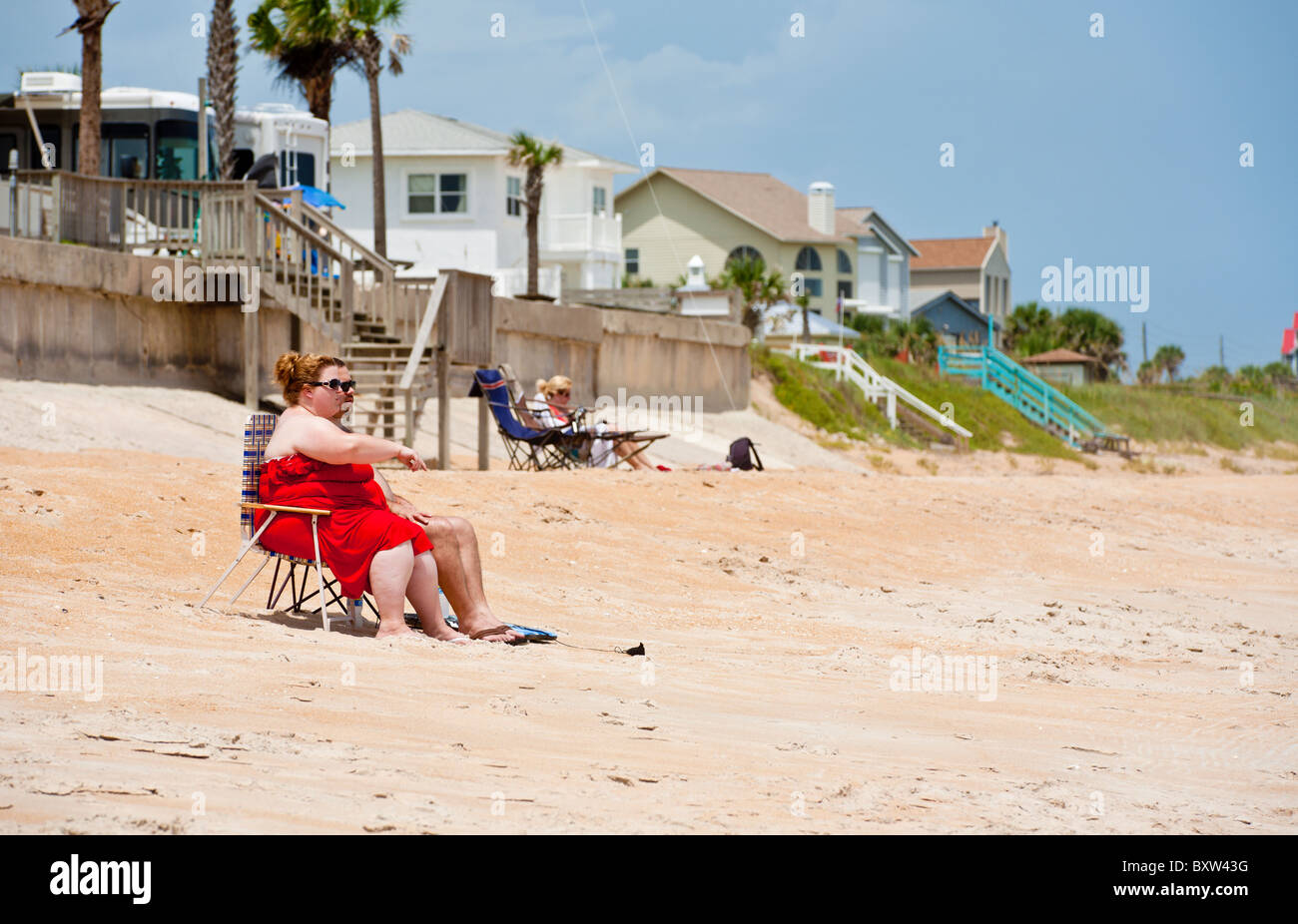 Obese woman in red sitting on chair sunbathing at Beverly Beach, Florida Stock Photo