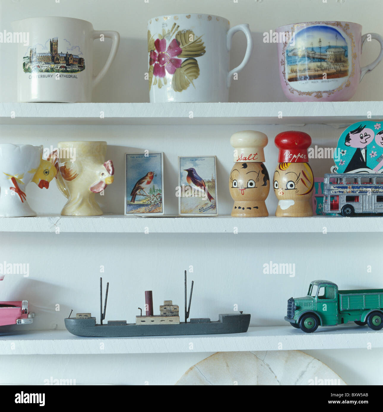 Close-up of collection of antique china cups with old metal toys and postcards on white shelves Stock Photo