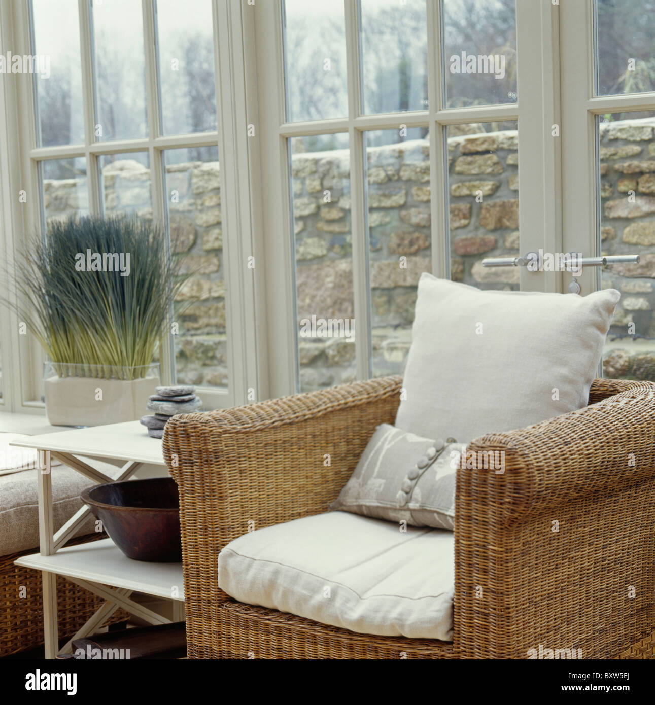 Cream cushions on wicker armchair in front of French windows in conservatory  living room Stock Photo - Alamy