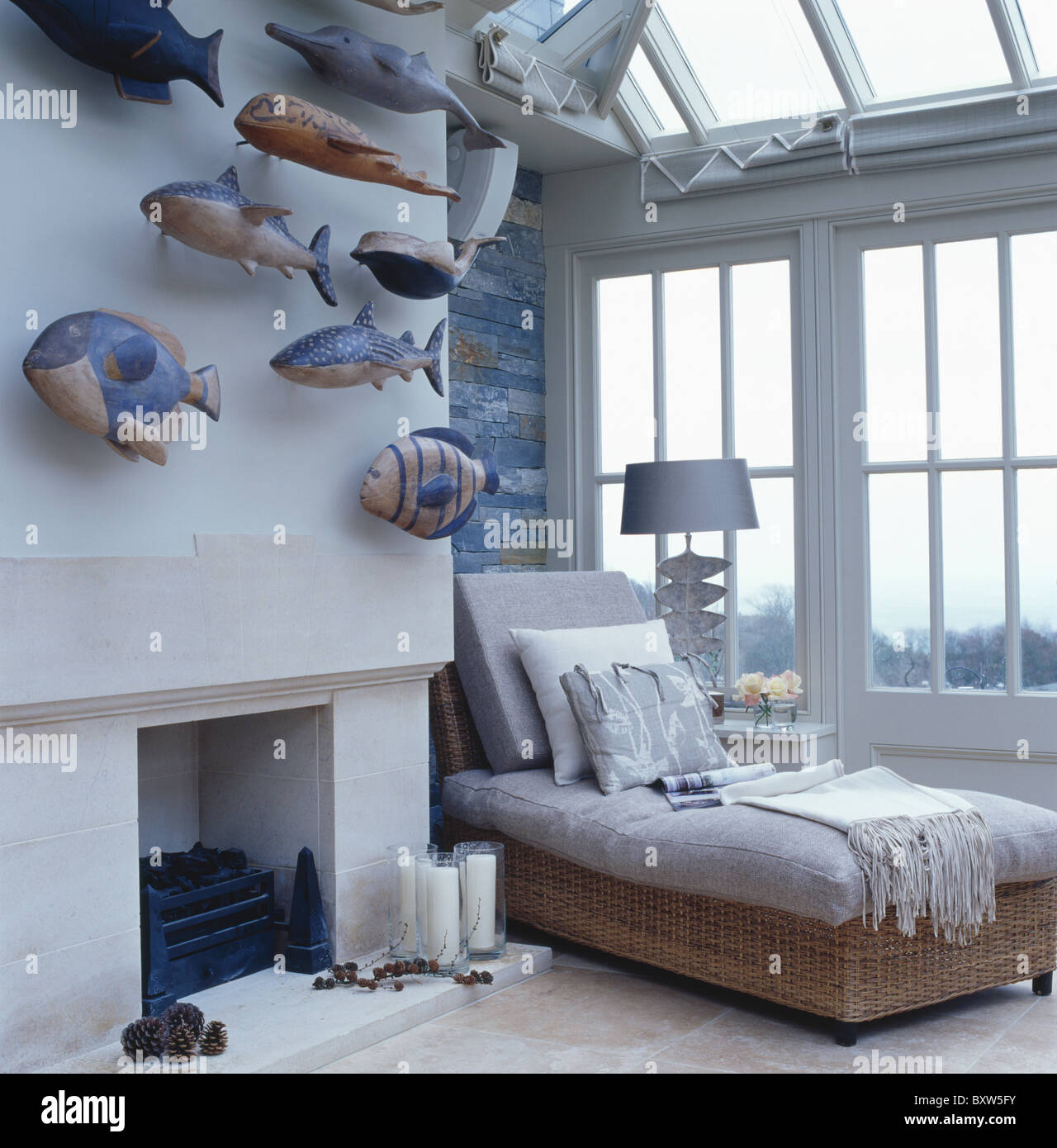 Collection of painted wooden fish above fireplace in loft conversion bedroom with gray day-bed in front of large window Stock Photo