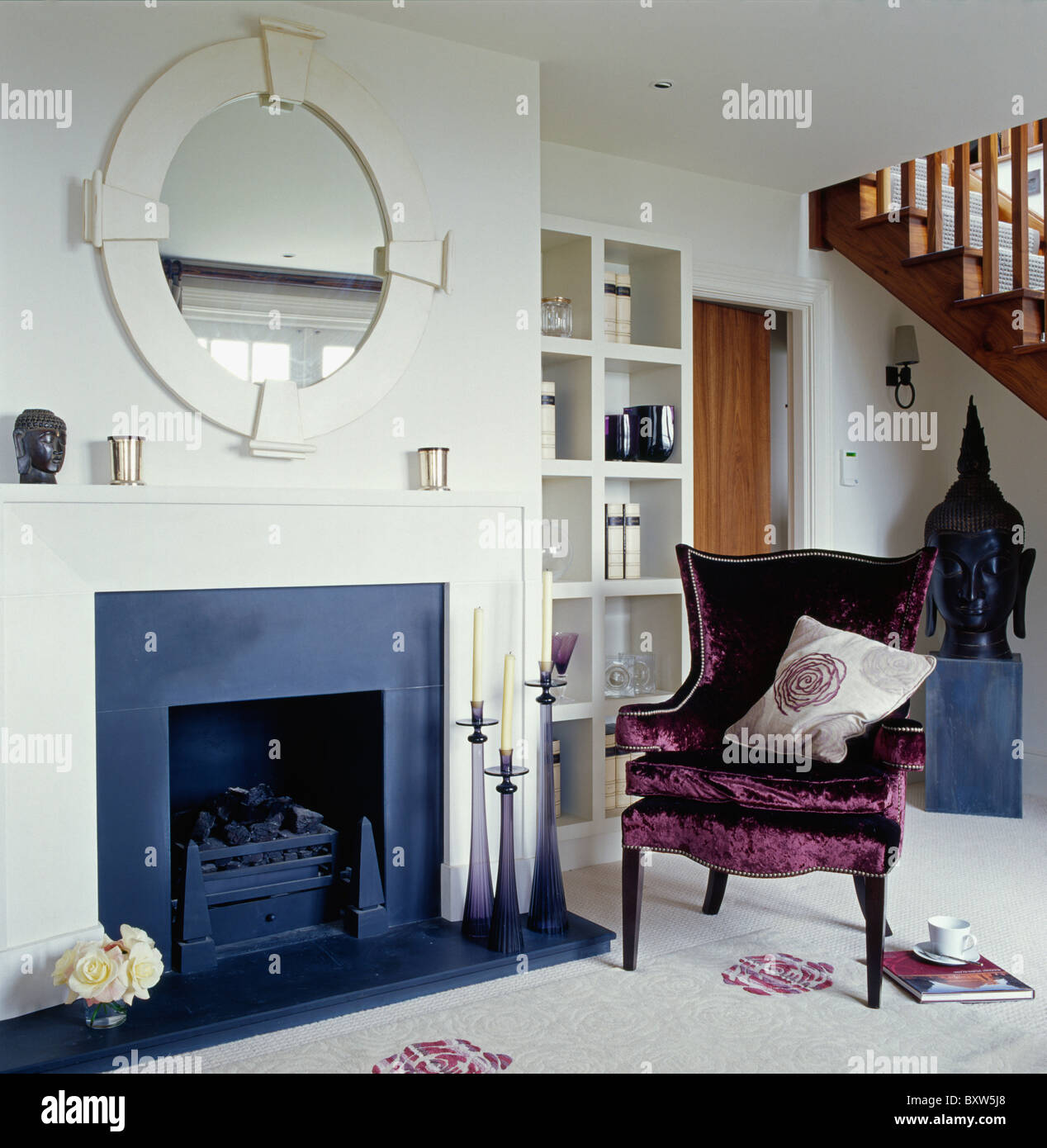 White circular mirror above fireplace in uncluttered white living room with purple velvet