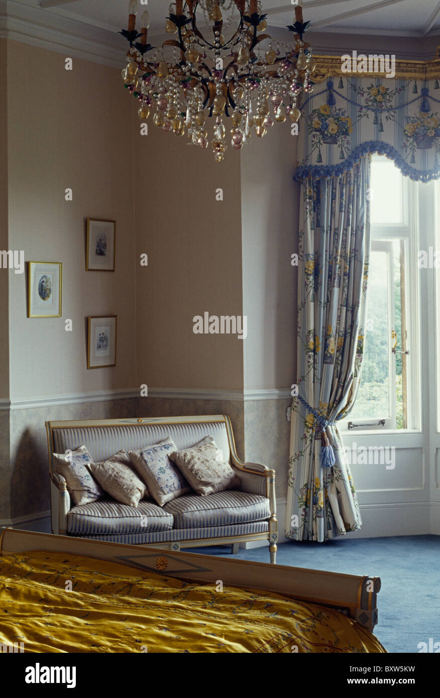 Grey silk-upholstered antique sofa in large country bedroom with antique glass chandelier Stock Photo