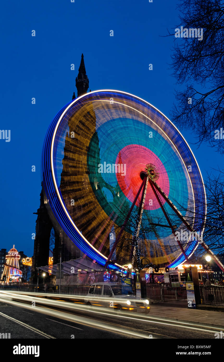 The Edinburgh Wheel in front of the Scott Monument with blurred traffic and taxi on Princes Street, Edinburgh, Scotland, UK. Stock Photo