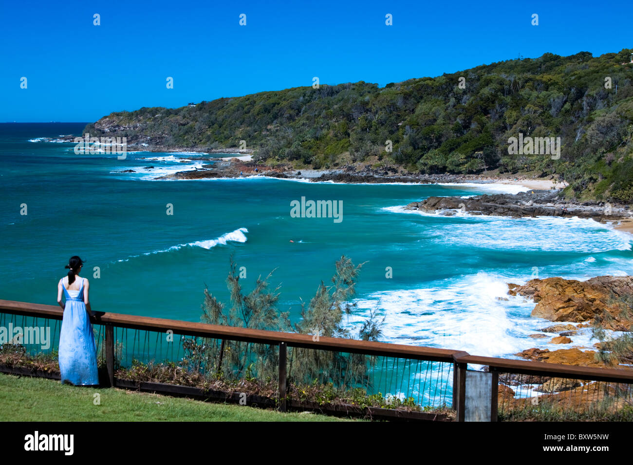 A young woman watches people surfing from cliff top vantage point at Point Perry Coolum Beach Queensland Australia Stock Photo
