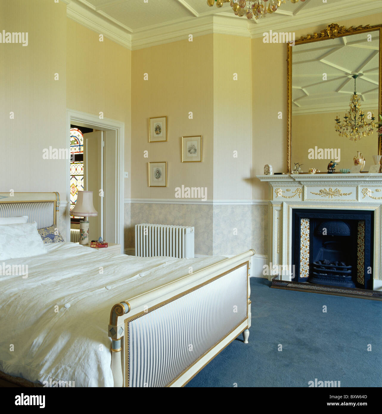 Large antique gilt mirror above fireplace in cream country bedroom with ...