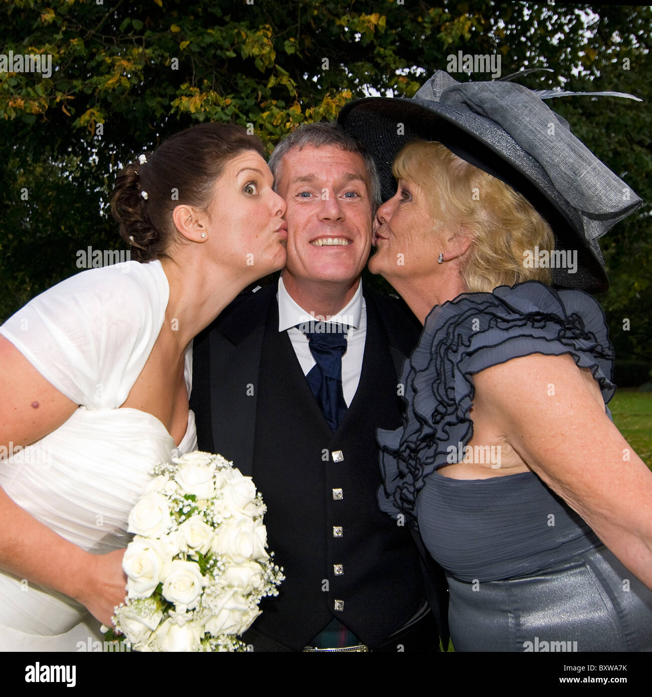 Square close up fun portrait of a groom on his wedding day getting a kiss on both cheeks from his new bride and mother-in-law. Stock Photo
