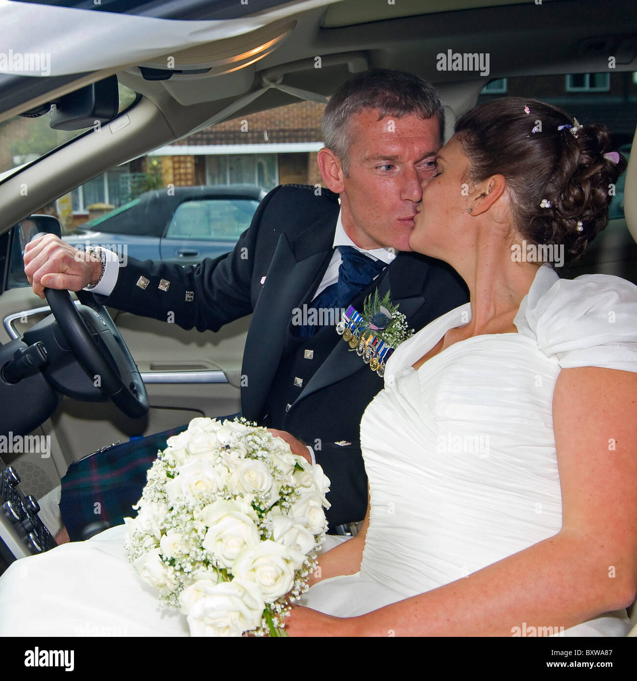 Square close up portrait of a bride and groom kissing in a car. Stock Photo