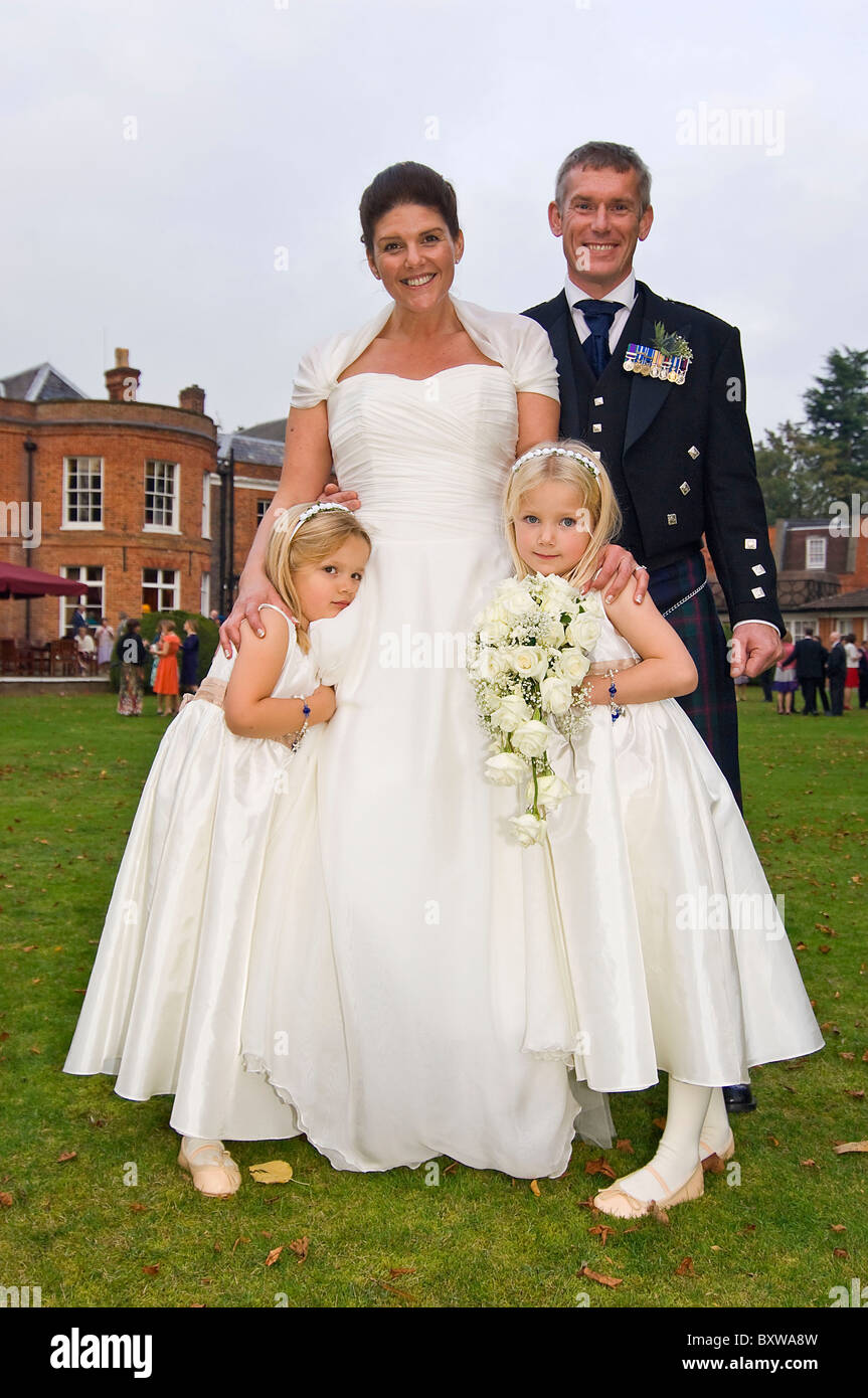 Vertical close up portrait of a bride and groom with their young flower girls posing for a photograph. Stock Photo