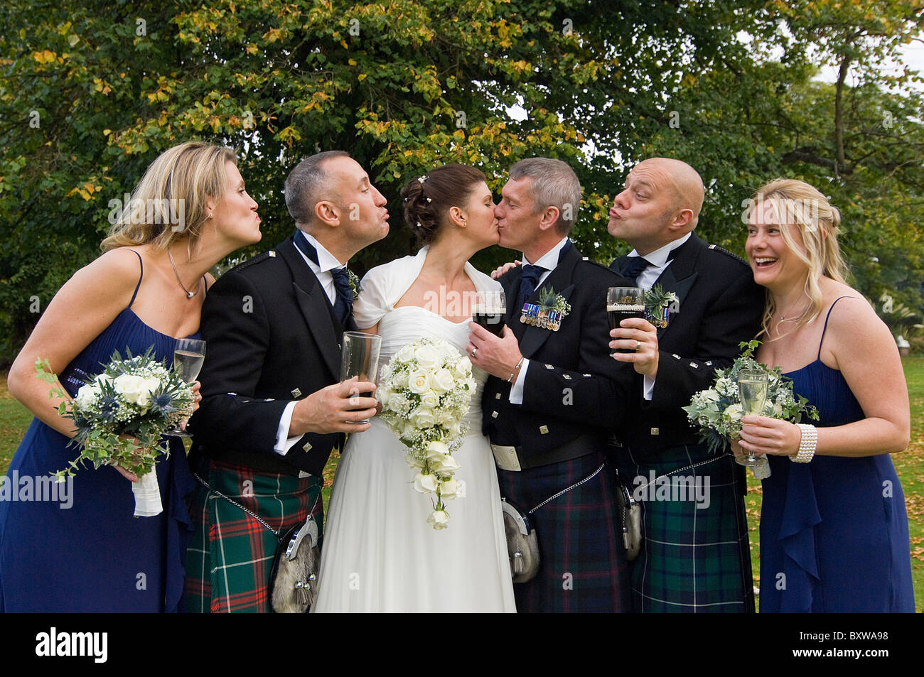 Horizontal close up portrait of a bride and groom kissing with their best men and bridesmaids pouting and mimicking them. Stock Photo