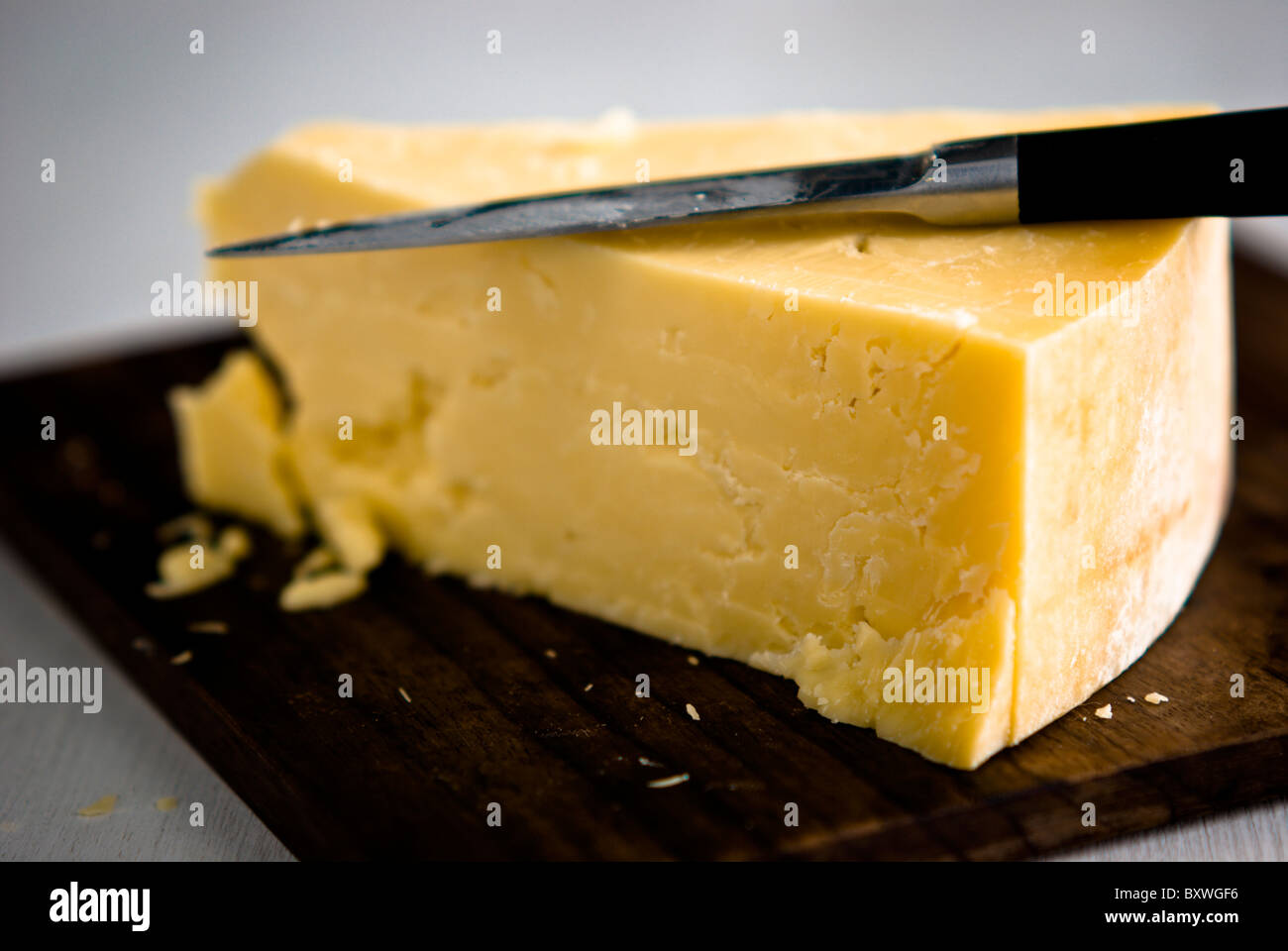 Wedge of cheddar cheese, being cut on wooden cheeseboard Stock Photo