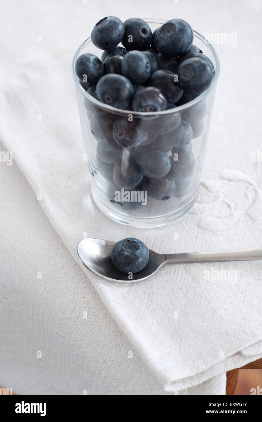 Small glass full of cultivated blueberries with single blueberry on teaspoon on old linen cloth Stock Photo