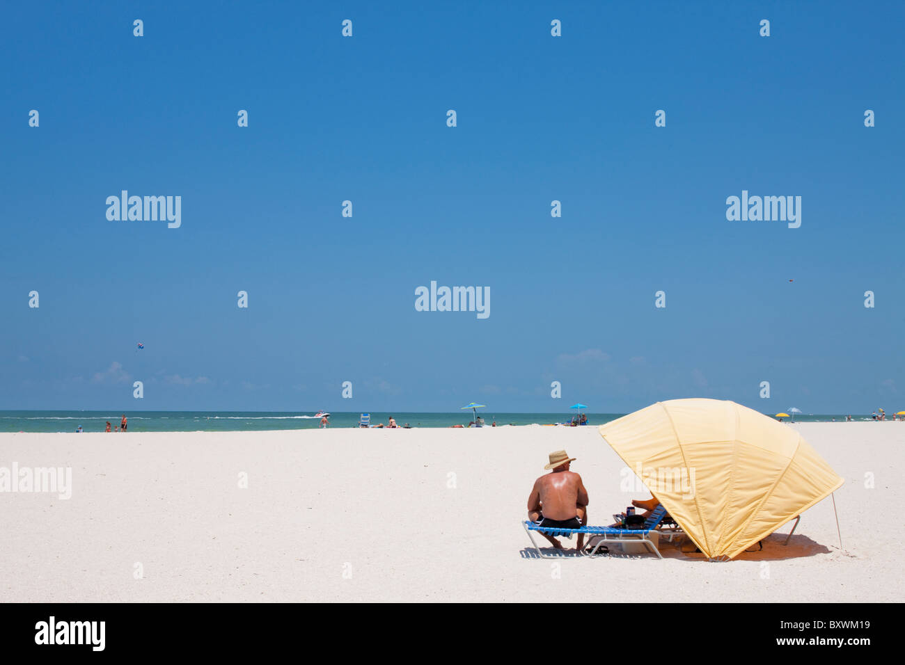 USA, Florida, St. Petersburg, Man sits sunbathing on white sand beach along Gulf of Mexico on summer morning Stock Photo