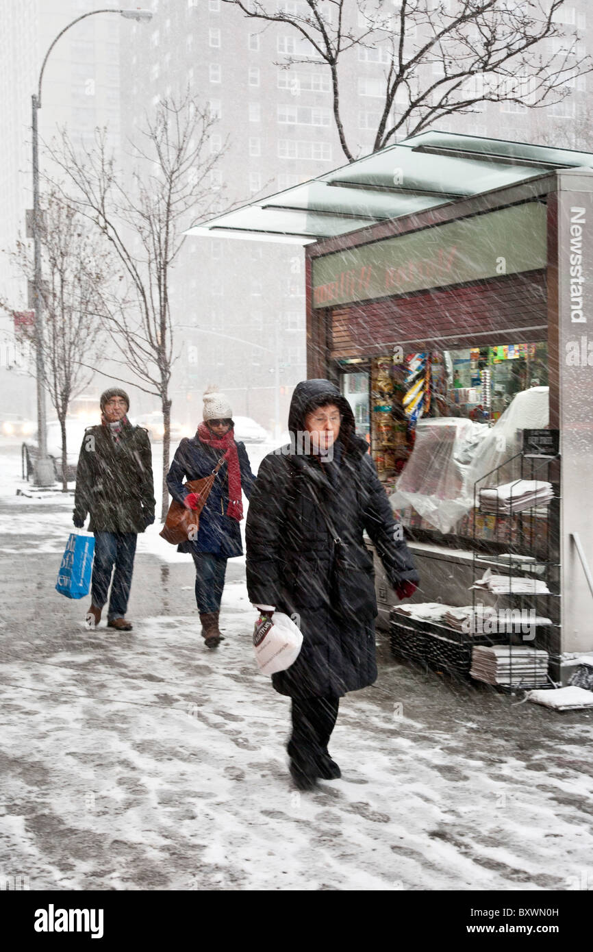 diverse bundled up pedestrians pass a brightly lit newsstand on ninth avenue as heavy snow falls during blizzard New York City Stock Photo