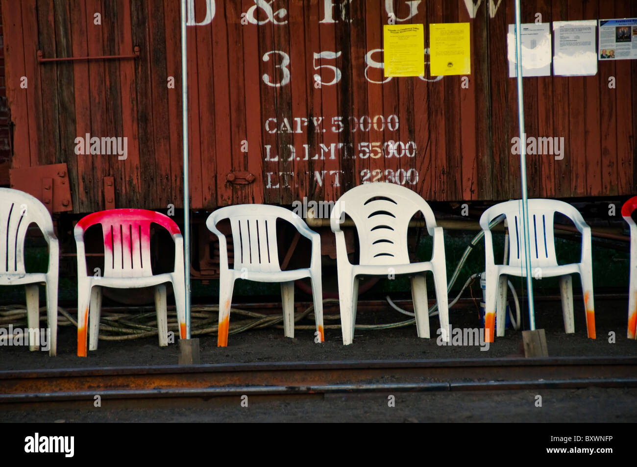 Row Of White Plastic Lawn Chairs In Front Of Train Boxcar