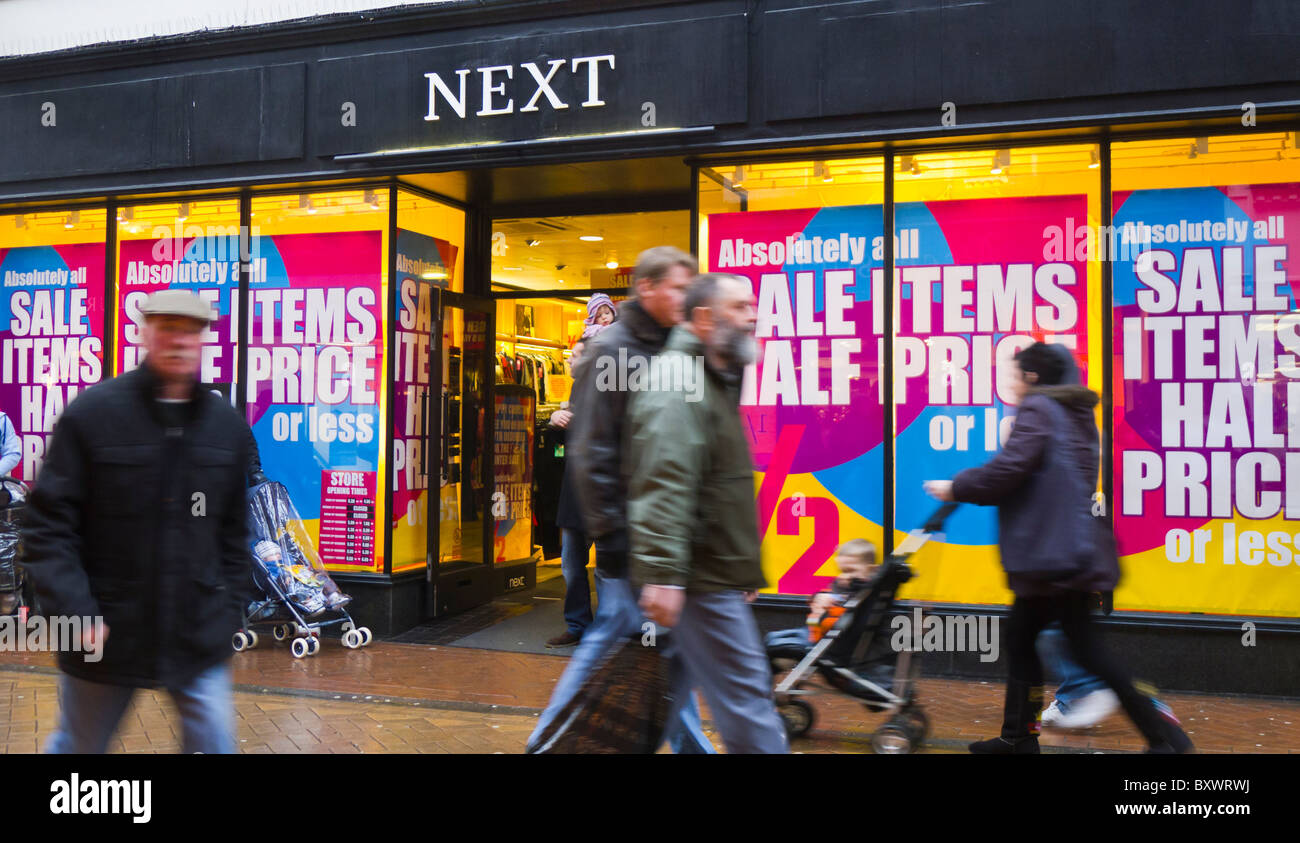 Shoppers on the high street passing infront of a Next store. Stock Photo