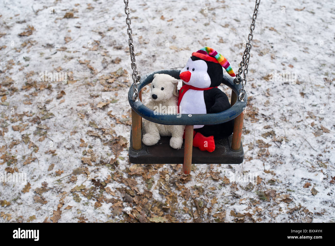 Stuffed toy polar bear and penguin in a swing on snowy ground. Stock Photo