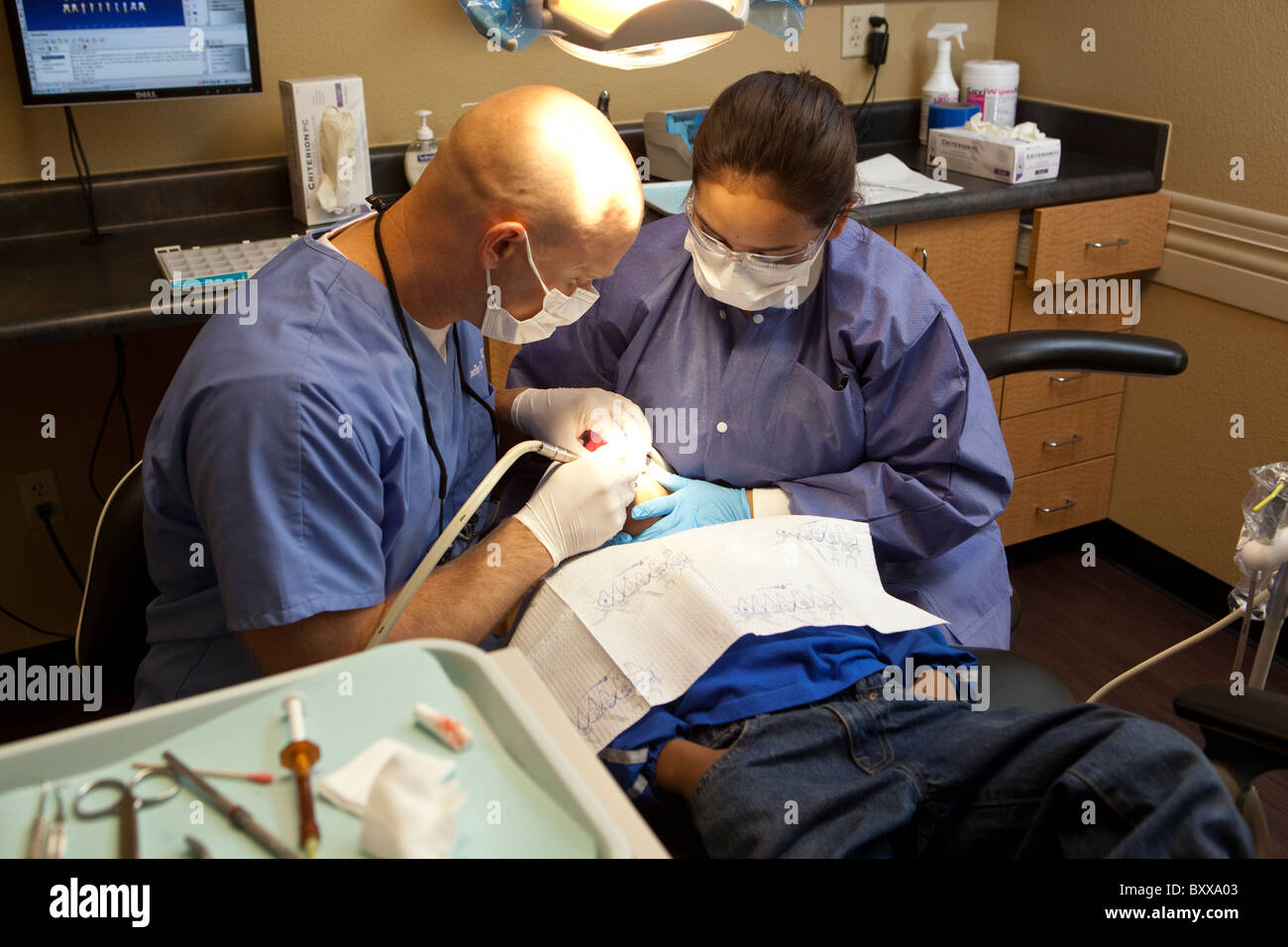 Anglo male dentist works on patient while female dental assistant looks on in treatment room of