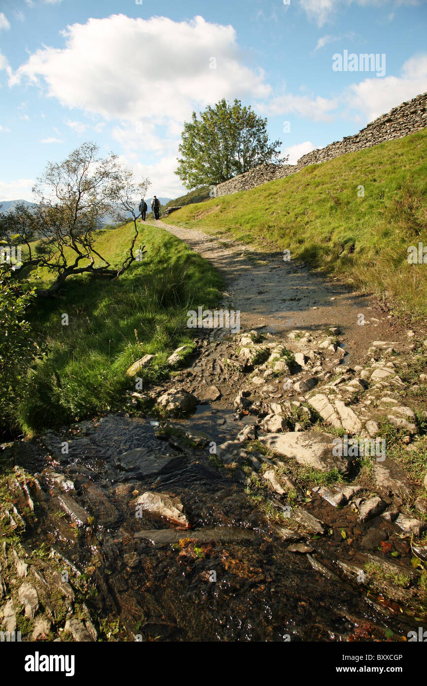 A country track with two people walking after crossing a stream with rocks Stock Photo